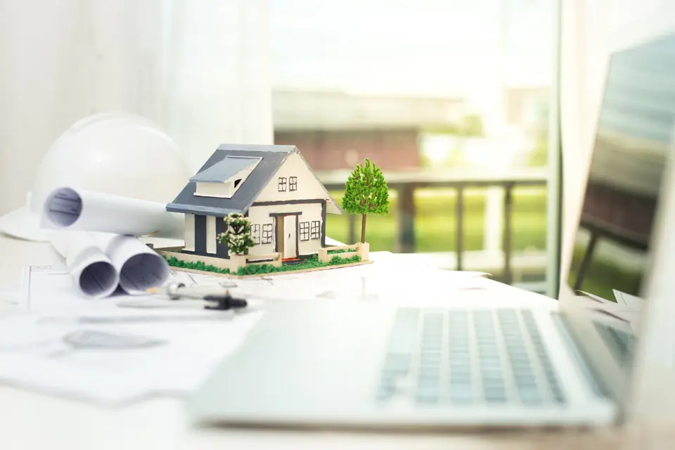 Model house on a desk beside building plans and a laptop